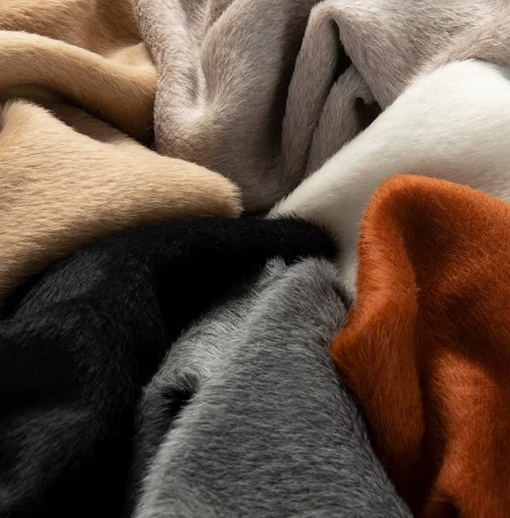 Fabrics in six luxurious colors, including Orchid White, Cognac, Carbon Grey, and Quicksand, being held to highlight their plush Suri alpaca texture. From Borcelleclothes.
