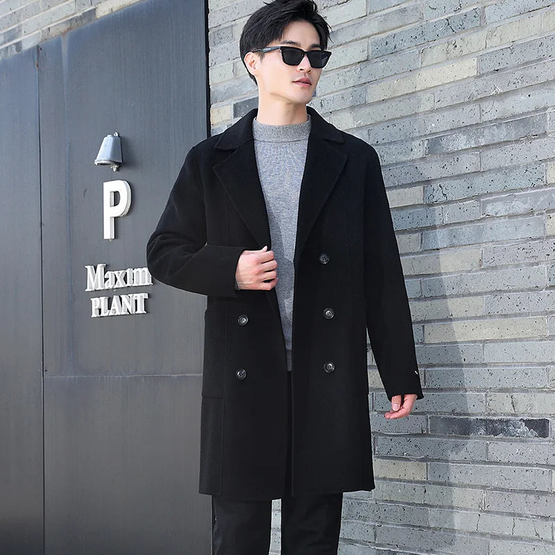 A model wearing the Men’s Double-Sided Wool Coat in Onyx, touching the front side, emphasizing its structured double-breasted design and classic tailoring. From Borcelleclothes.