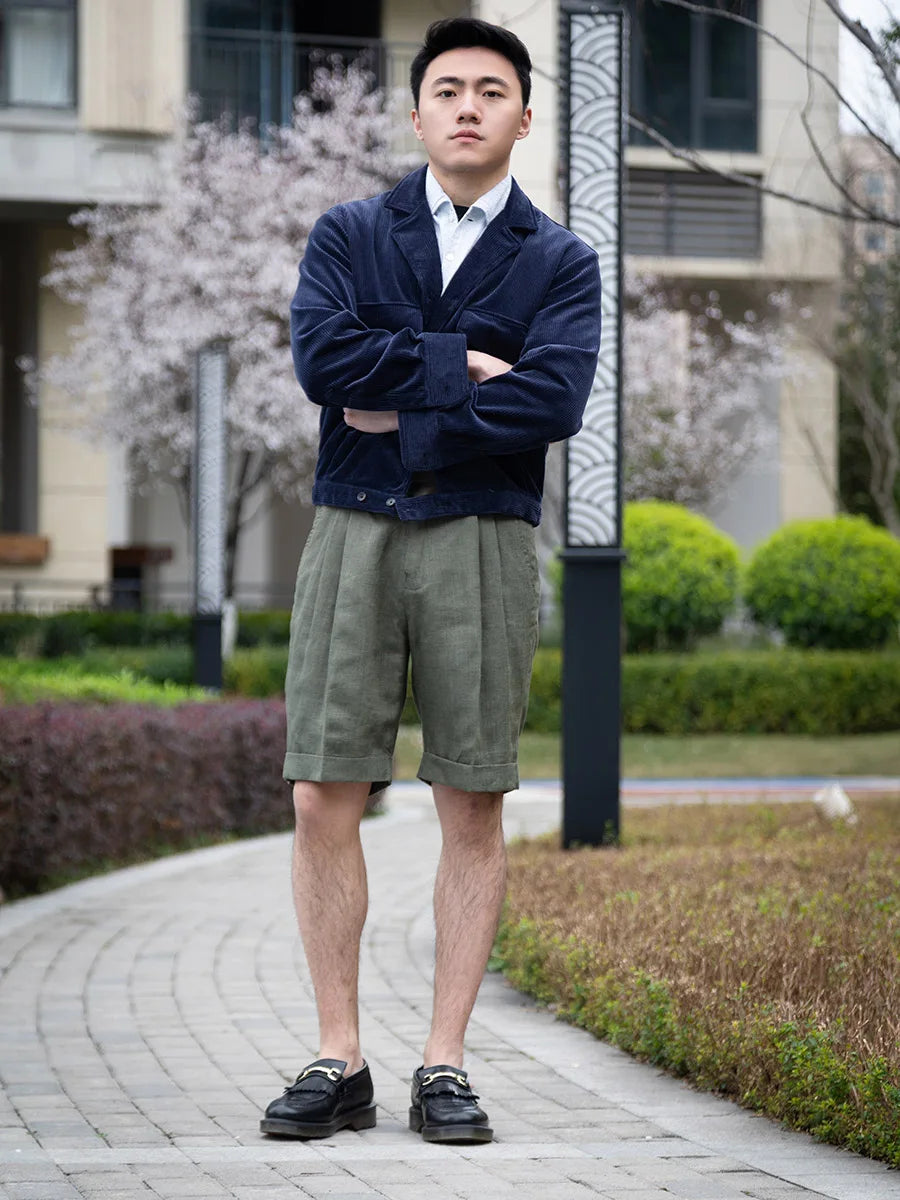 Model standing with arms crossed, wearing sage linen shorts styled for modern summer elegance. From Borcelleclothes.