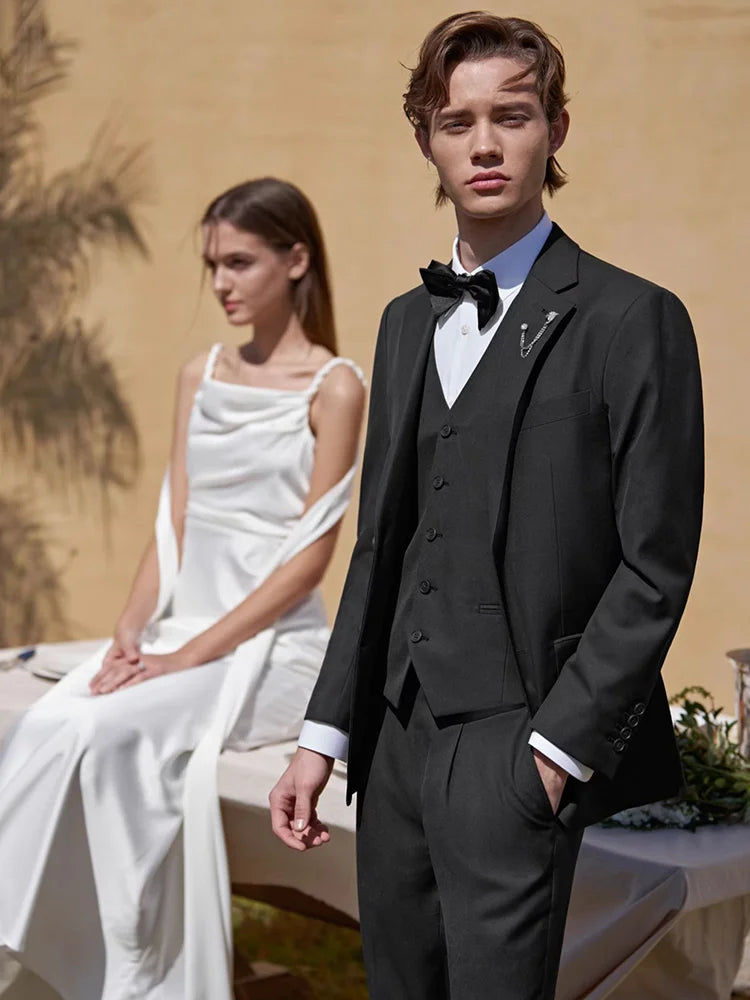 Model in a black wool-blend suit with the bride in soft focus behind, capturing a ceremonial moment. From Borcelleclothes.