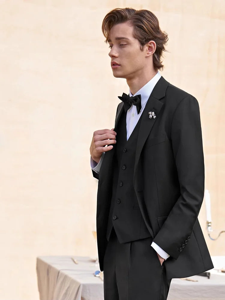 Model in a black suit touching the lapel with one hand and resting the other in his trouser pocket. From Borcelleclothes.
