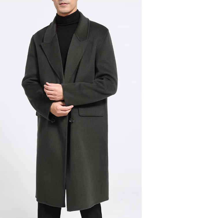 A model wearing the Men's Peaked-Lapel Wool Coat in Tuatara, touching the sleeve end, emphasizing the structured sleeve and fine craftsmanship. From Borcelleclothes.
