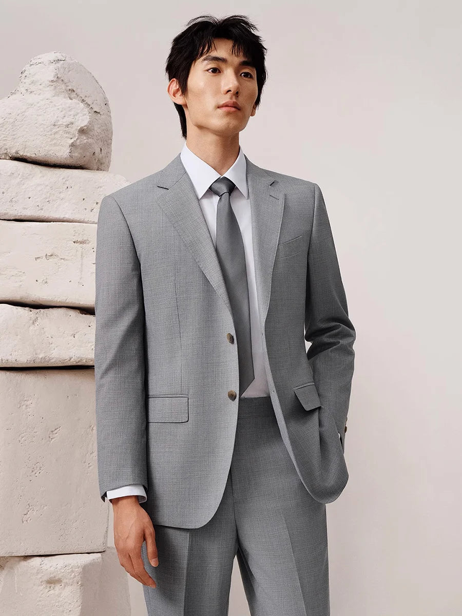 Model standing before stone wall, dressed in French Grey suit with refined silhouette. From Borcelleclothes.