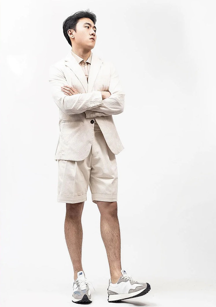 Model in Swiss Coffee tailored shorts standing casually with left foot raised on the heel, reflecting effortless poise. From Borcelleclothes.