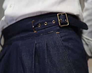 Detailed view of the left waistband construction showing hidden belt strap with brass buckle on denim trousers. From Borcelleclothes.