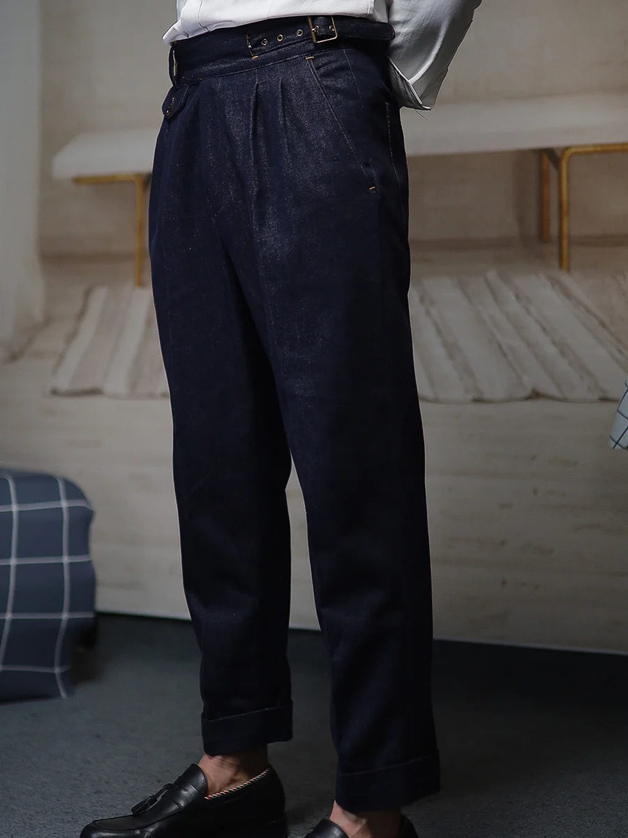 Model stands with hands behind back, showing the pleated front and structured silhouette of the tailored denim trousers. From Borcelleclothes.