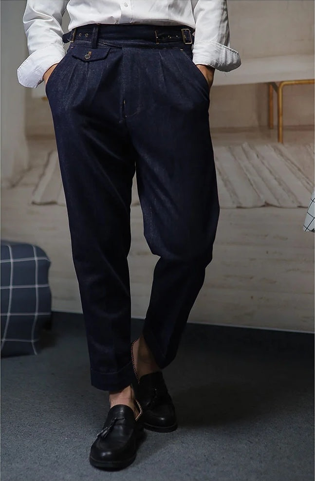 Men's tailored denim trousers in Midnight Express with four front pleats, dual side buckles, and contrast stitching. From Borcelleclothes.