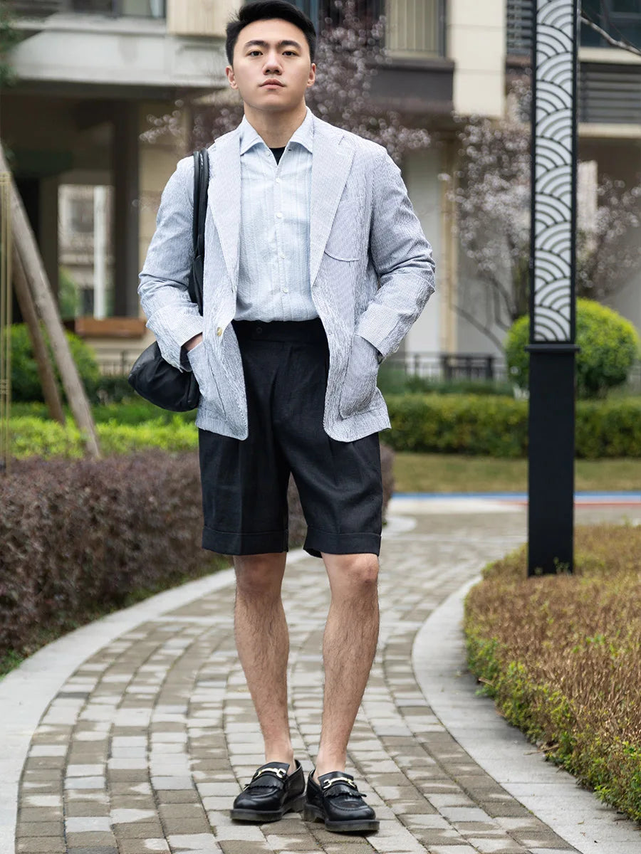 Model stands in onyx linen tailored shorts and blazer, hands resting in the blazer pockets, exuding understated confidence. From Borcelleclothes.