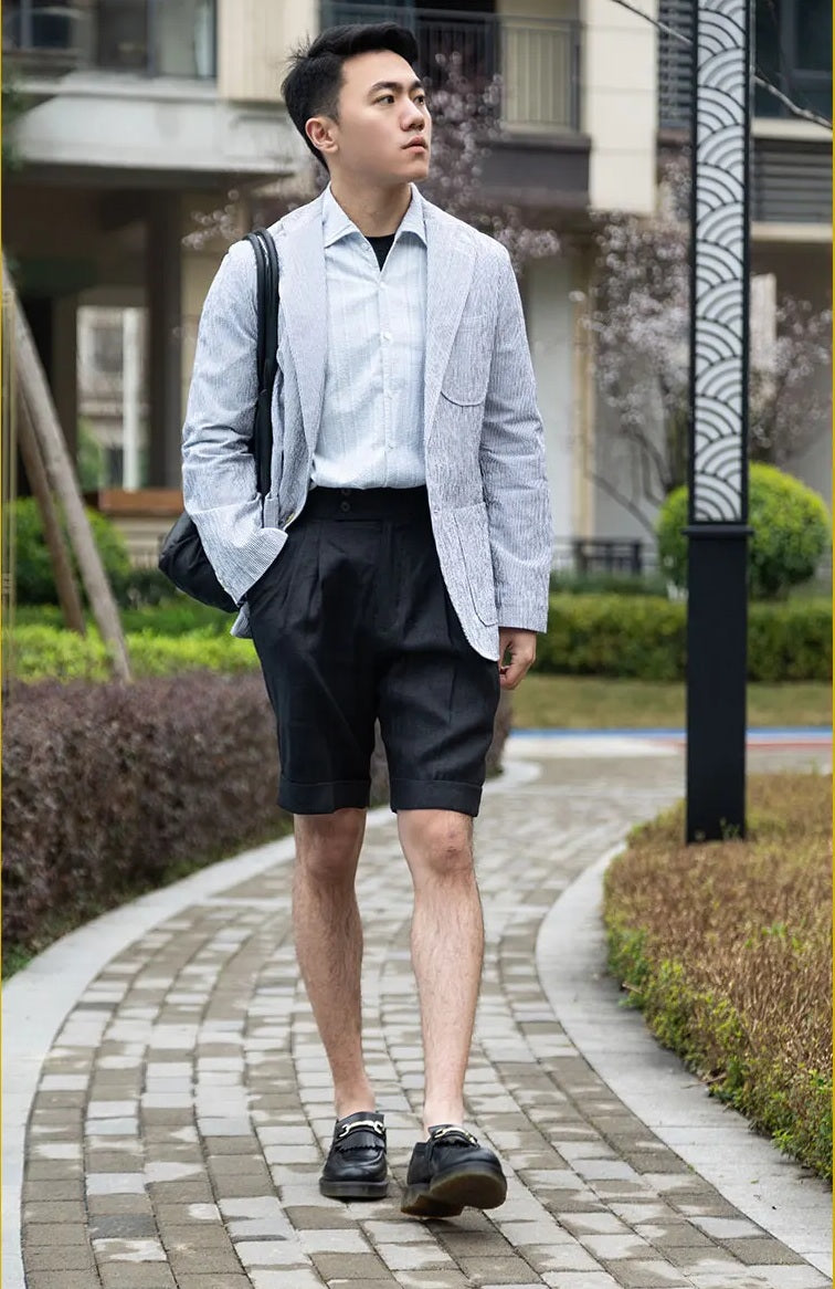 Model walks forward in onyx linen tailored shorts, the movement emphasizing the structured drape of the linen. From Borcelleclothes.