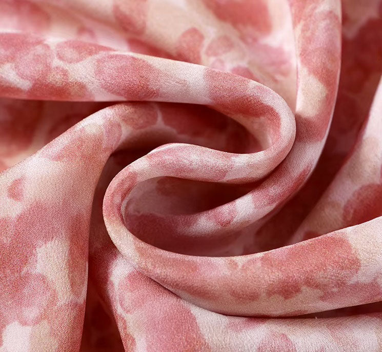 Abstract floral Mulberry silk chiffon fabric in soft pink tones, delicately draped to reveal its airy texture and watercolor-inspired pattern. From Borcelleclothes.