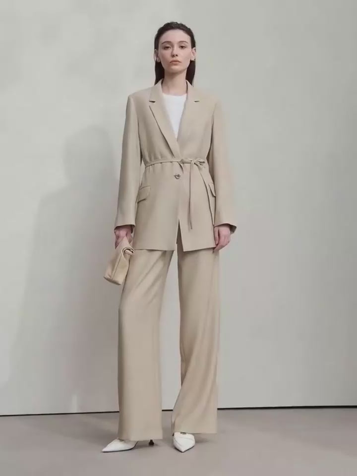 Video showcasing a Women’s crinkled viscose blazer in Soft Amber, Morning Blue, and Onyx colors, with deep textured folds, notch lapels, flap pockets, sculptural triangular button, and belt threaded through side openings. From Borcelleclothes.