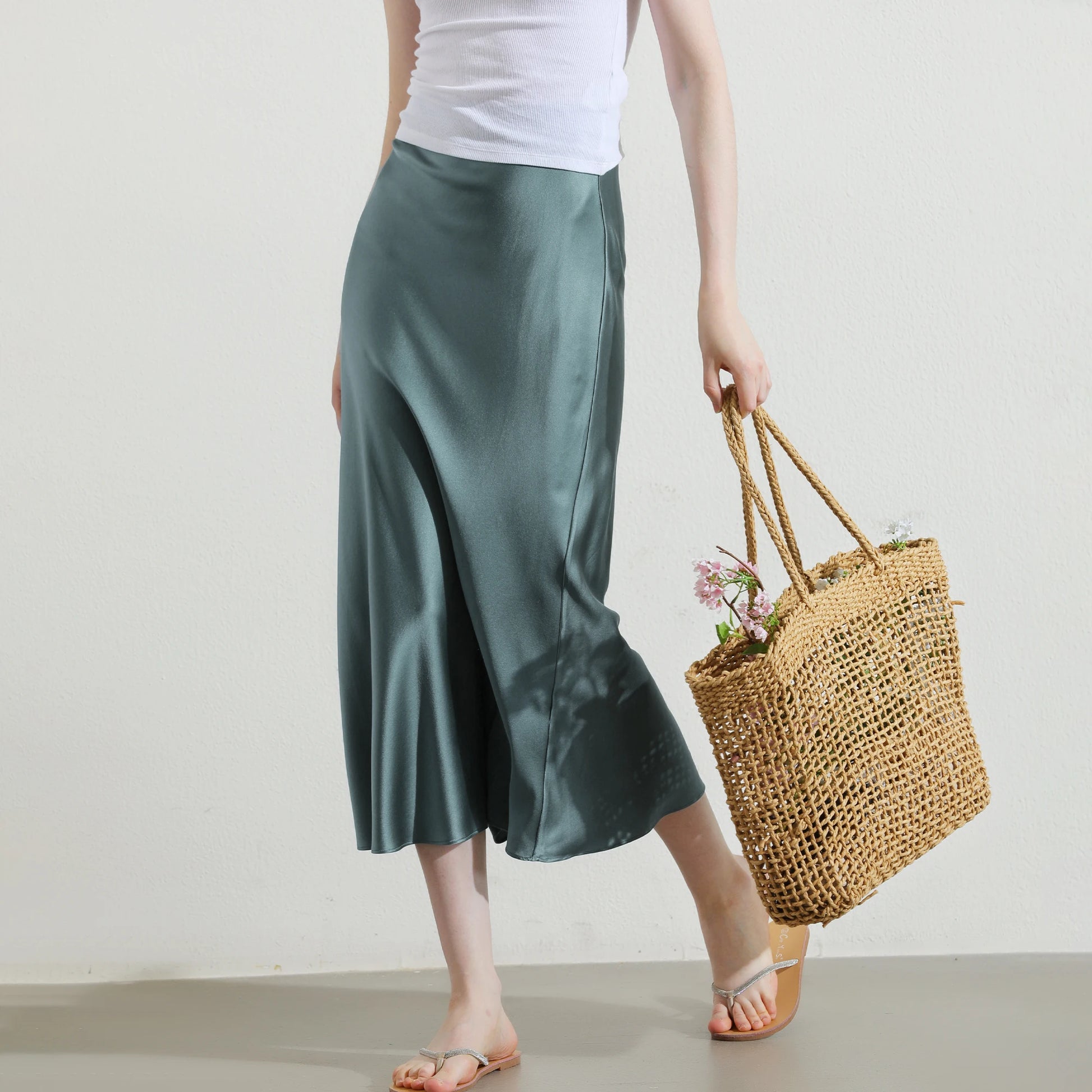 Model in Blue Bayoux silk skirt holding soft neutral bag with flowers inside, styled with quiet elegance. From Borcelleclothes.