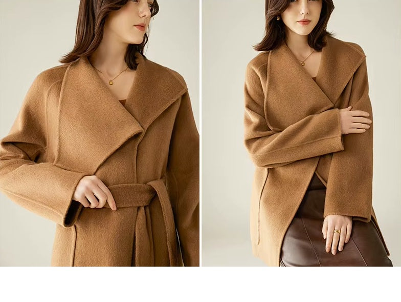 A model wearing the Women's Asymmetrical Camel Hair Coat in Bourbon, seated in a chair, showcasing its structured yet effortless elegance. From Borcelleclothes.