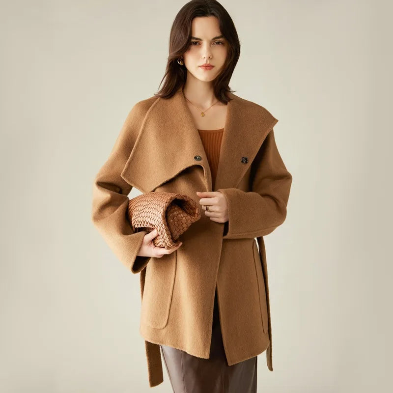 A model wearing the Women's Asymmetrical Camel Hair Coat in Bourbon, holding a bag, emphasizing its versatile styling and effortless sophistication. From Borcelleclothes.