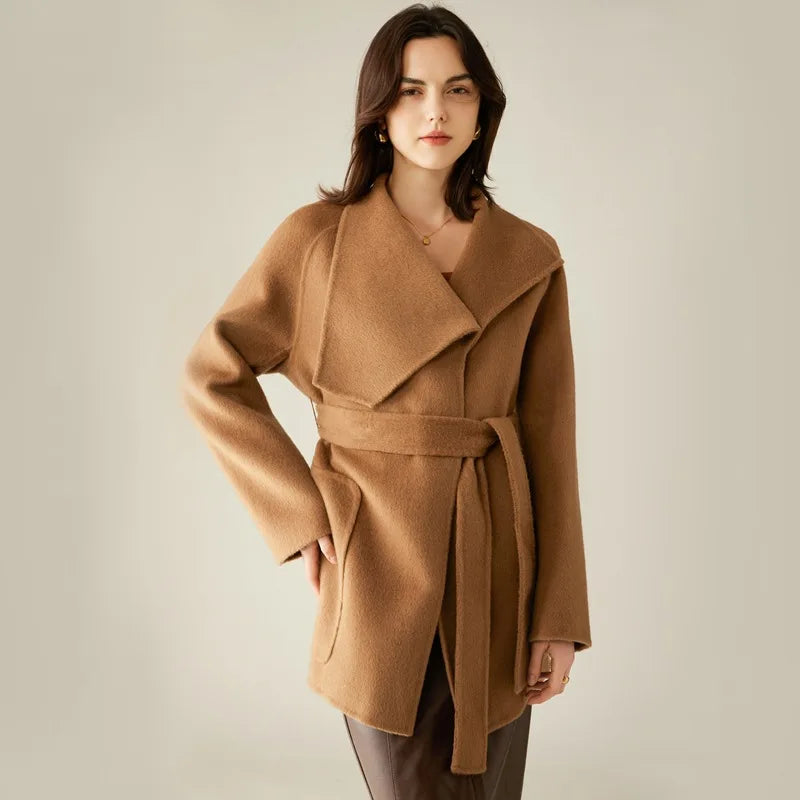 A model wearing the Women's Asymmetrical Camel Hair Coat in Bourbon, touching the pocket, highlighting its seamless integration into the structured design. From Borcelleclothes.
