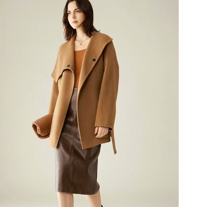A model wearing the Women's Asymmetrical Camel Hair Coat in Bourbon, turned slightly to the side, highlighting the asymmetrical lapels and fluid drape. From Borcelleclothes.