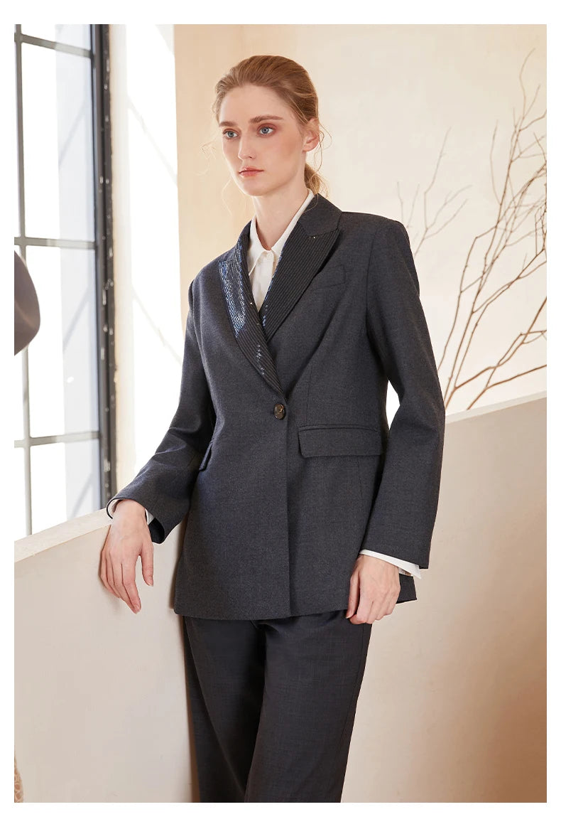 Women’s Australian wool blazer in Davy Grey with chain detail, model by white staircase with one hand on hip. From Borcelleclothes.