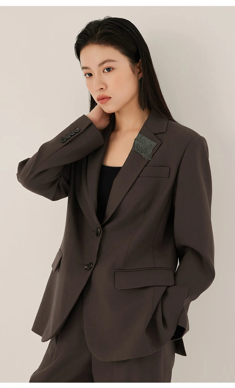 Woman in black chocolate blazer with rhinestone fringe detail, touching her neck – from Borcelleclothes.