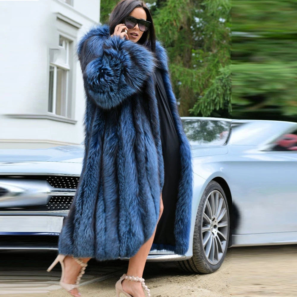 A woman in a sweeping Calypso silver fox fur coat descends a staircase, the coat’s flowing length mirroring her poised and effortless presence. From Borcelleclothes.