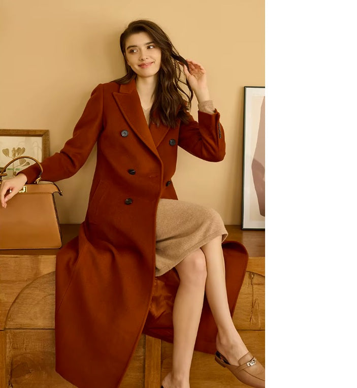 Model in the Women's Cashmere Blend Long Coat in Rust Brown, seated on a sofa, showcasing the bold, vibrant hue and flowing silhouette. From Borcelleclothes.