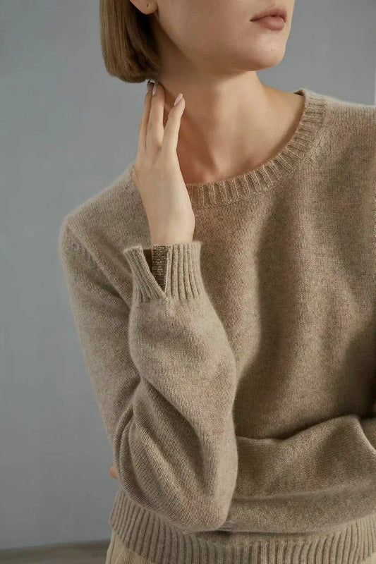 Women’s slim-fit cashmere sweater in Sandrift, with ribbed cuffs and subtle metal accents. Model touching her neck — From Borcelleclothes.