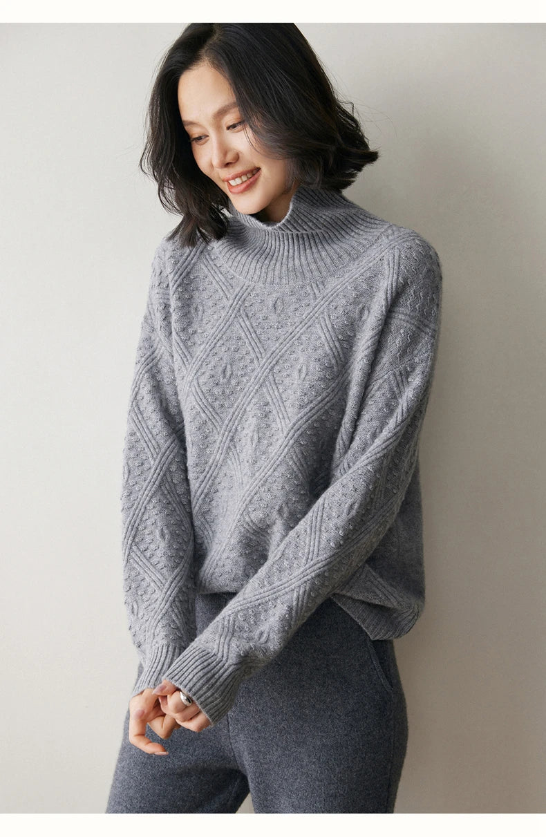 Model gently touching the cuff of a French Grey cashmere sweater with airy diamond motif — From Borcelleclothes.