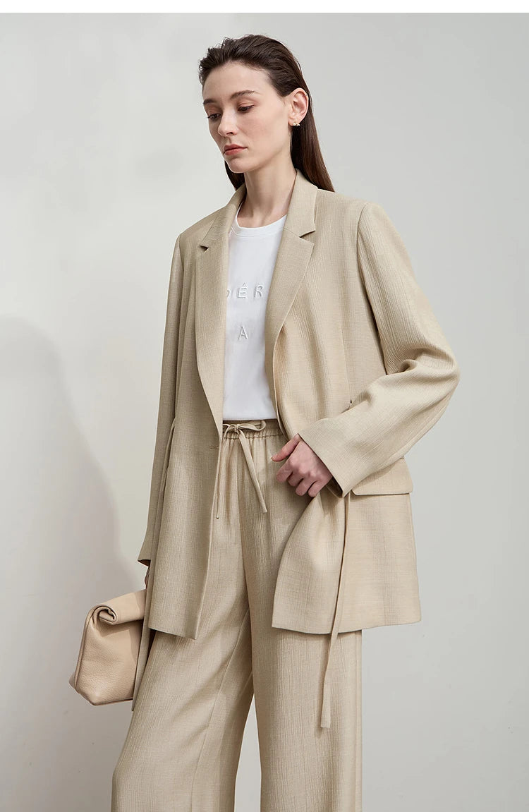 Woman touching front side while wearing unfastened Soft Amber crinkled viscose blazer – From Borcelleclothes.