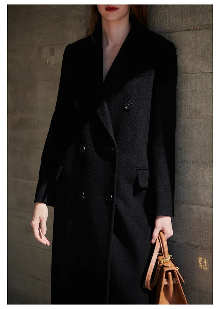 Woman in an Onyx cashmere wool coat standing near a textured stone wall. From Borcelleclothes.