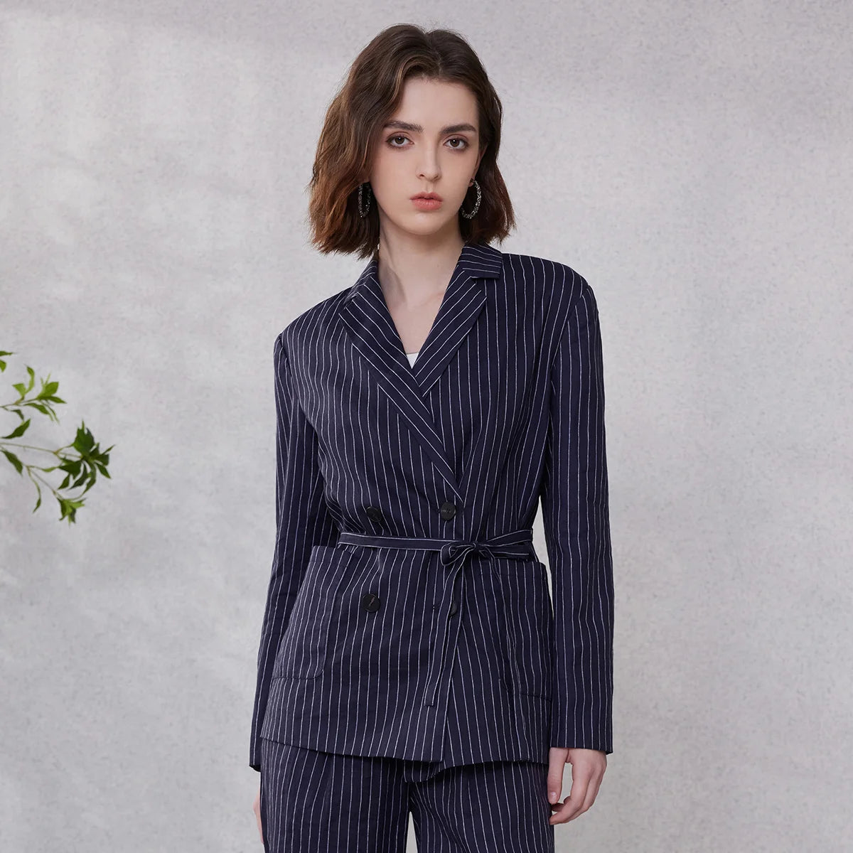 Woman in Mirage blue ramie blazer with wide stripes, hand placed behind back, showing double-breasted cut and waist belt – From Borcelleclothes.