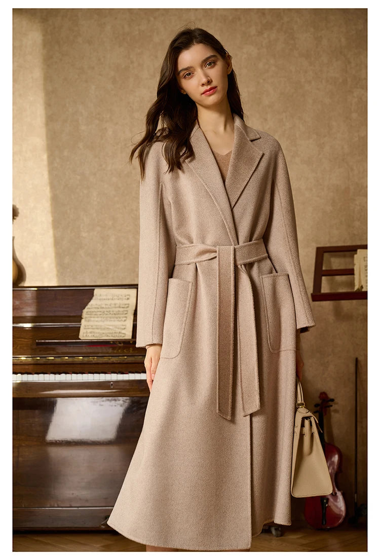 Model wearing a sandrift double-sided cashmere wrap coat, standing in front of a piano. From Borcelleclothes.