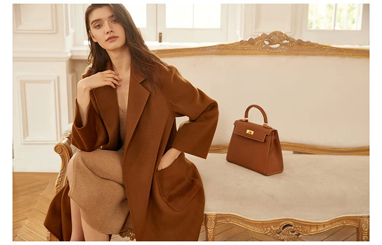 Model wearing a sienna double-sided cashmere wrap coat, sitting on a sofa. From Borcelleclothes.