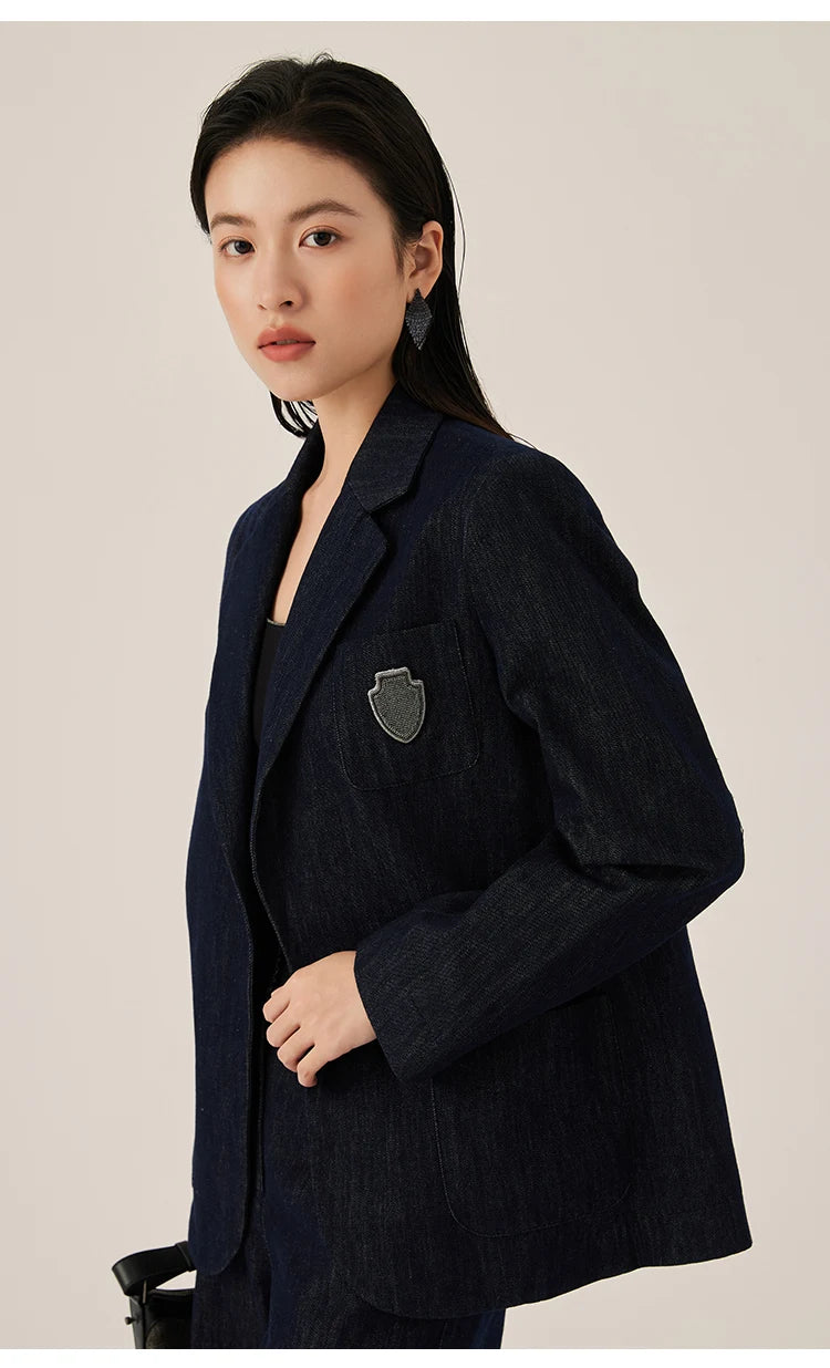 Ebony Clay denim blazer with model touching front side, highlighting open-front design and badge detail – From Borcelleclothes.