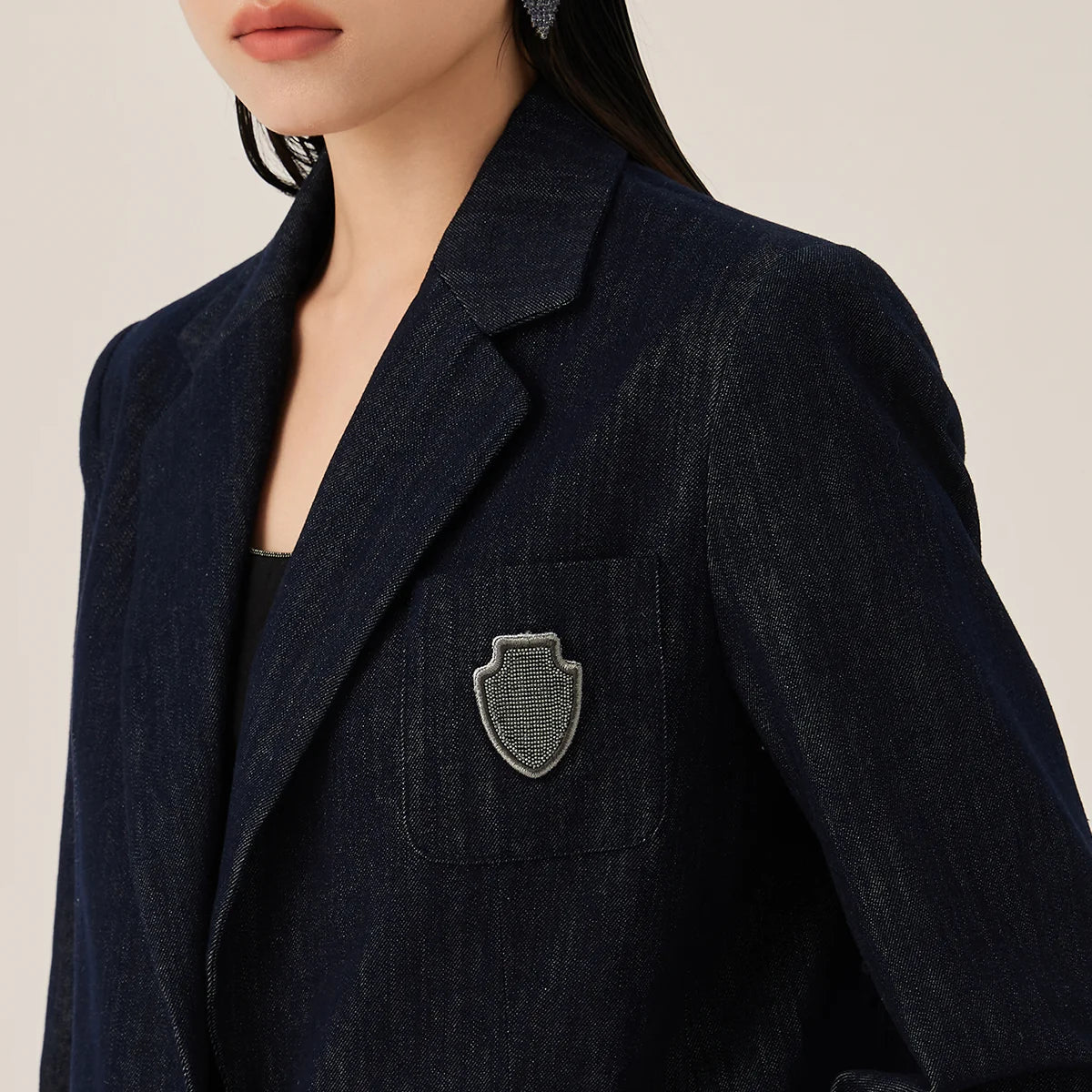Close view of the upper part of Ebony Clay denim blazer with rhinestone badge on chest pocket and structured shoulders – From Borcelleclothes.