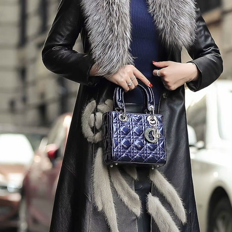 Women's Goatskin Down Coat in Onyx. Model holds bag in front, showcasing the belted waist and structured fit. Borcelleclothes.