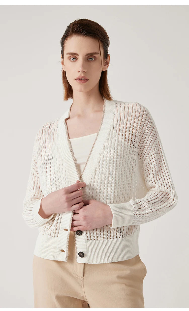 Woman wearing Wild Sand linen cardigan, gently touching the side trim, showing contrast edge and vertical lace knit. From Borcelleclothes.