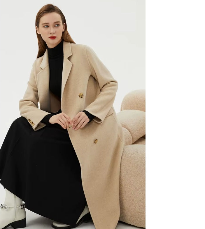 Model sitting and gazing to the side in the Women's Minimalist Long Wool Coat in Vanilla, highlighting its flowing design and mid-calf length. From Borcelleclothes.
