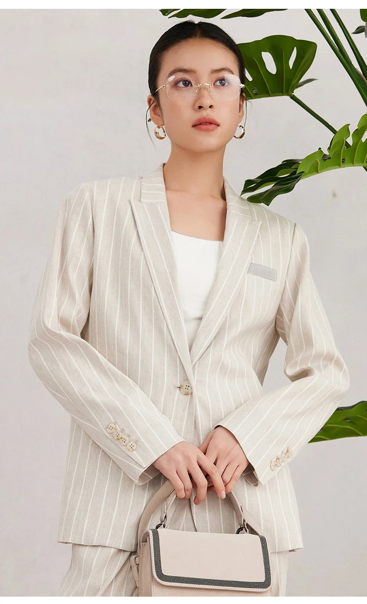 Front view of the model in Pearl Bush striped blazer holding a small bag with both hands, combining structure with softness. From Borcelleclothes.