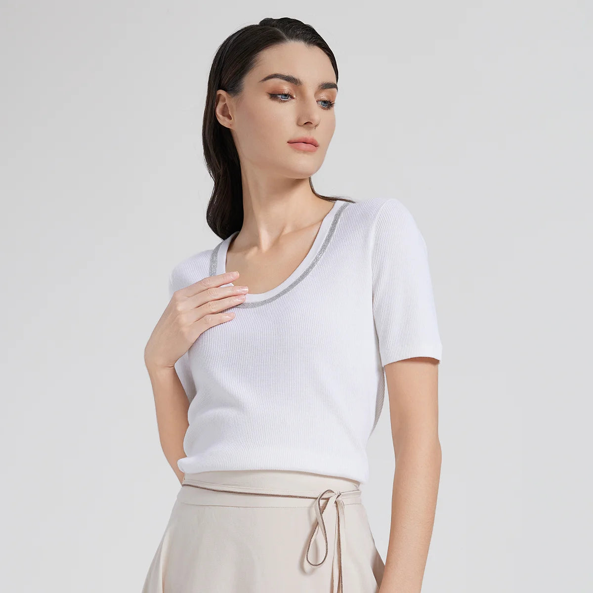 Woman softly touching the rhinestone-trimmed neckline of her White Lilac top, highlighting the delicate shimmer and elegant curve. From Borcelleclothes.
