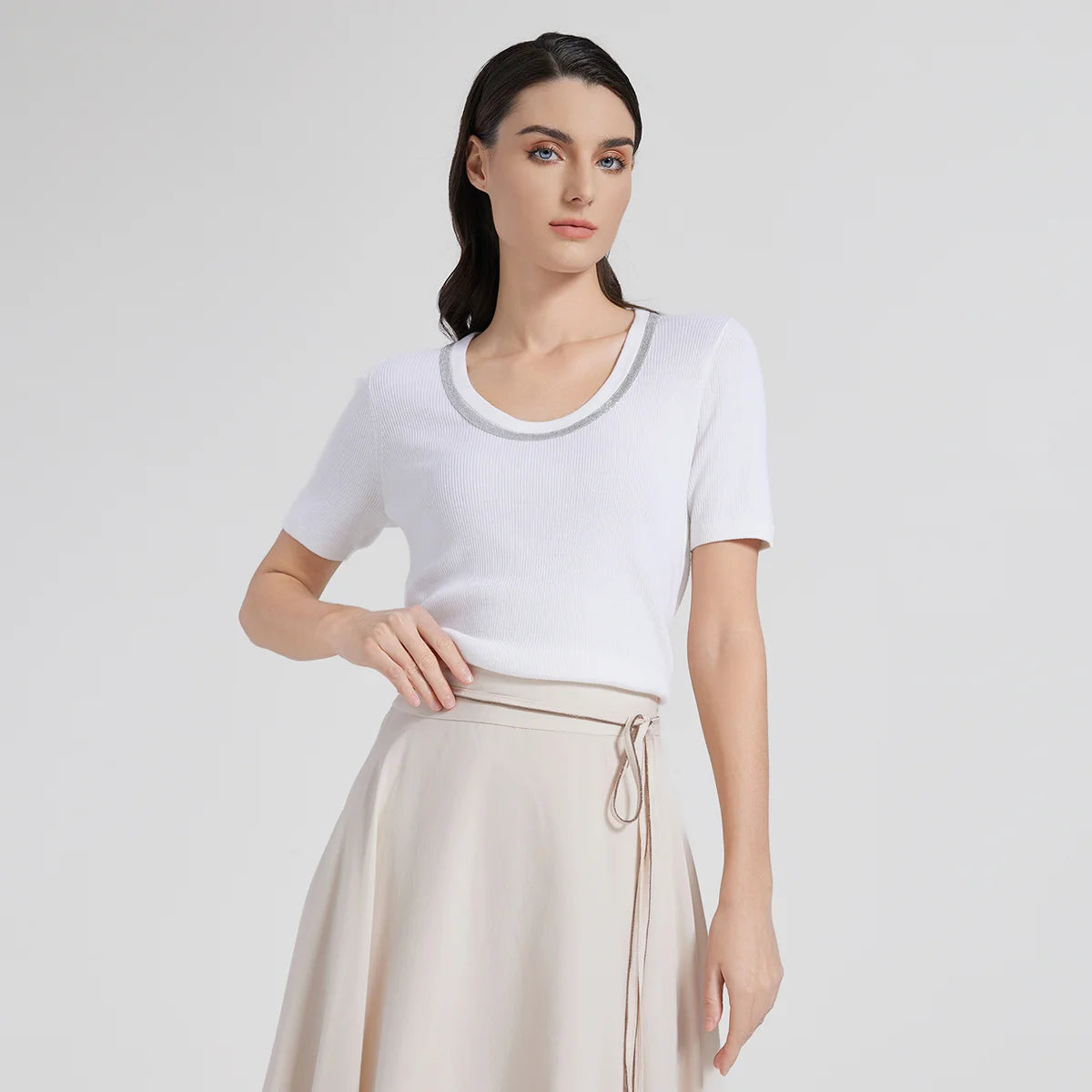 Woman gently touching the waistband of her skirt while wearing the White Lilac top, revealing graceful posture and fabric drape. From Borcelleclothes.