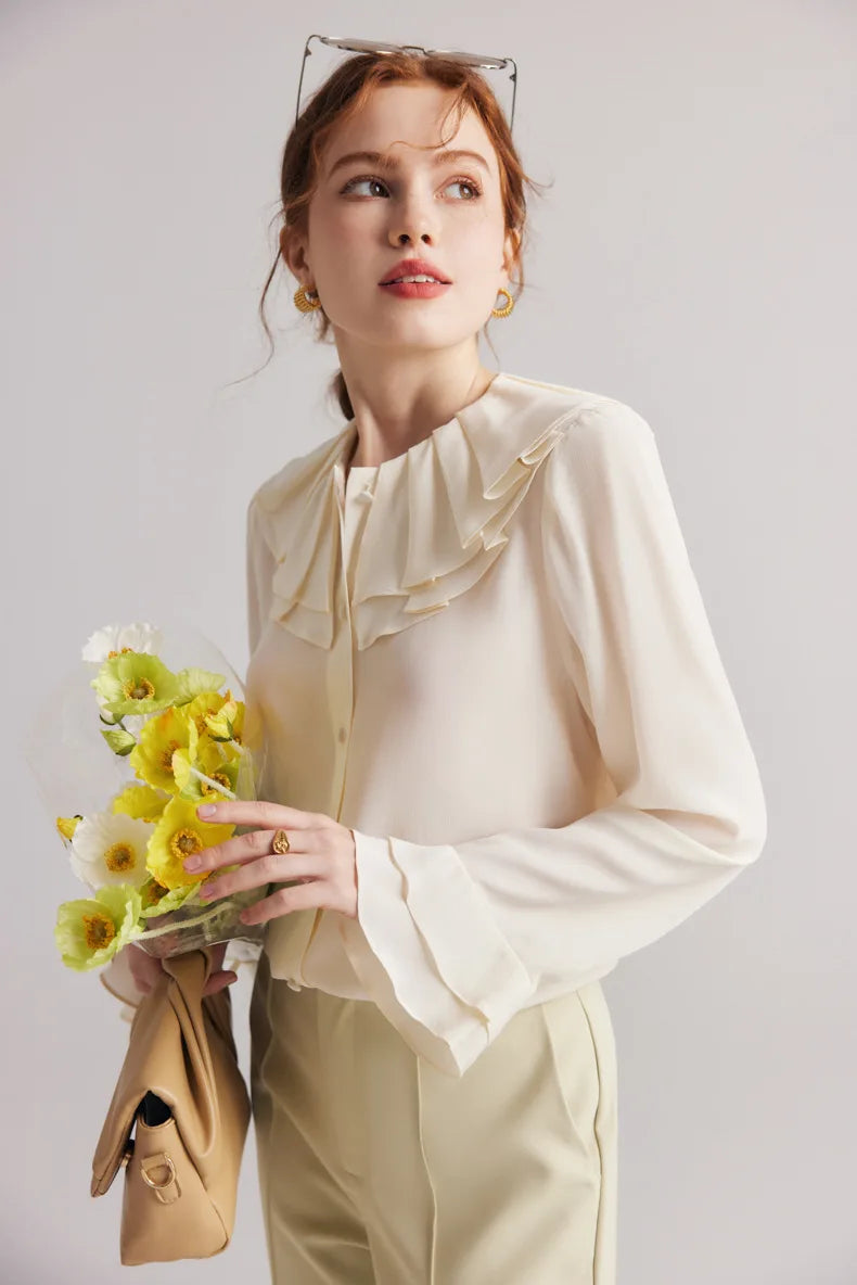 Model in the Women's Romantic Pearl Bush Silk Blouse touching flowers. From Borcelleclothes.