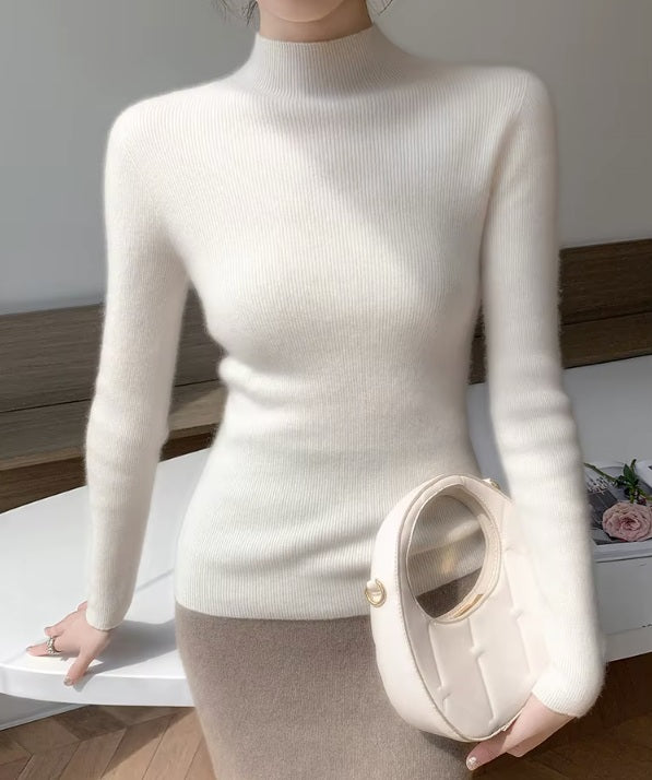 A model perched on the edge of a table, wearing the women's Saddle Sleeves Cashmere Sweater in Spring Wood, highlighting its sleek silhouette and modern design, Borcelleclothes.