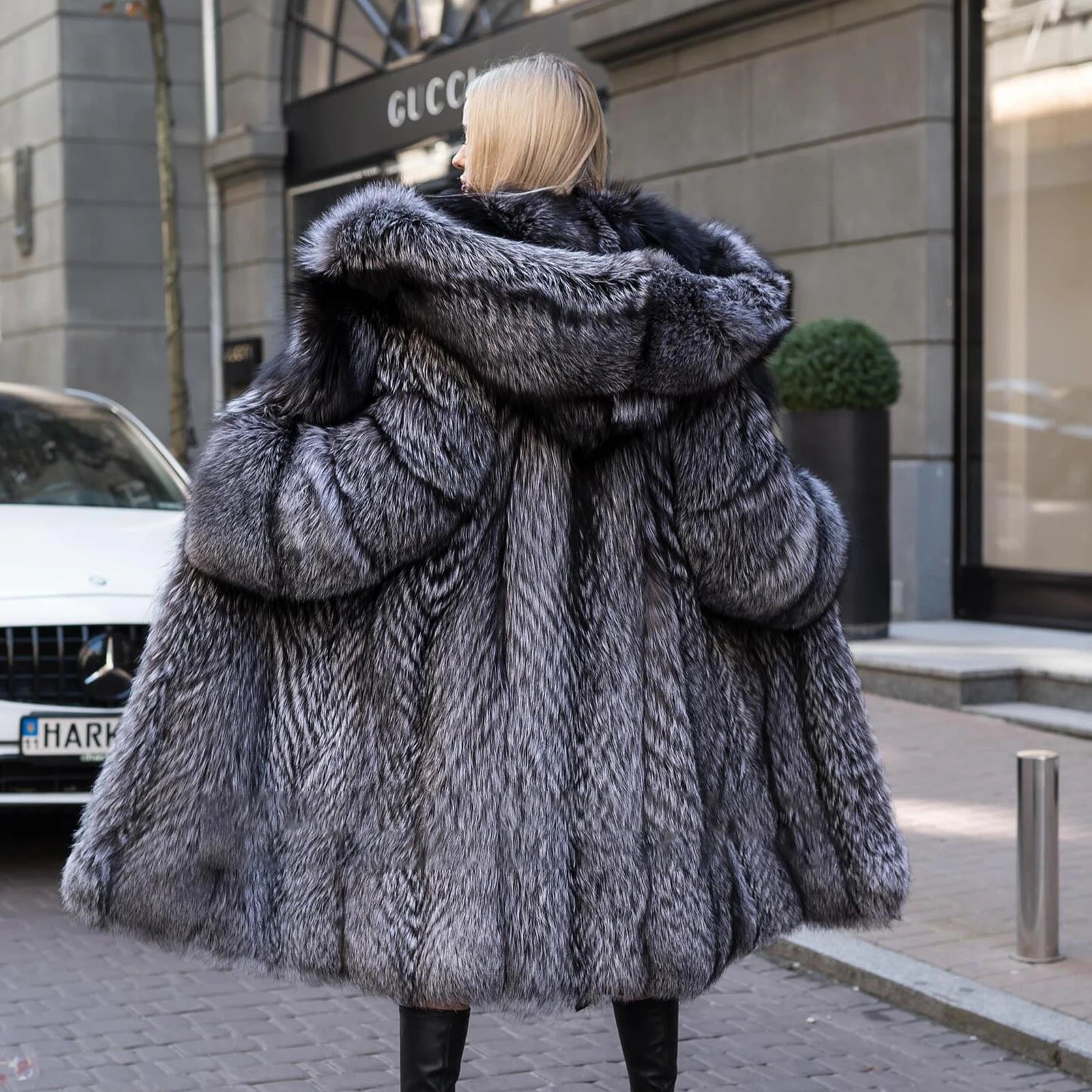 A model wearing a Women's Silver Fox Fur Coat, focused from the rear view, stretching the front sides to reveal its effortless fluidity and enveloping presence. From Borcelleclothes.