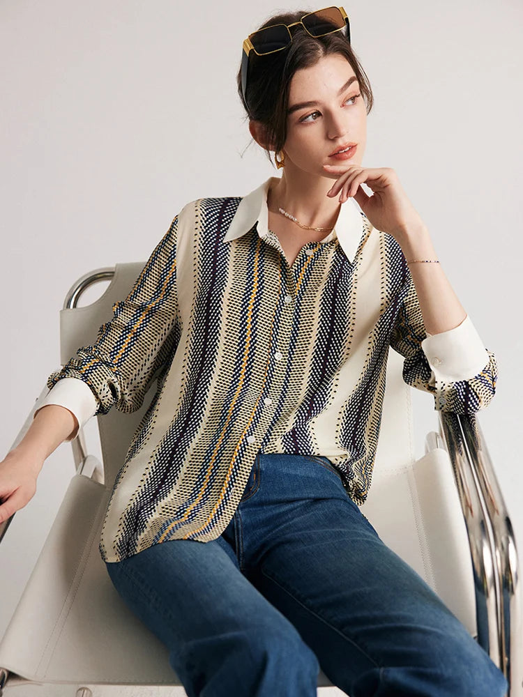 Model sitting on a chair wearing a striped 3D geometric silk shirt with bold orange, blue, and yellow stripes, showing a relaxed fit. From Borcelleclothes.