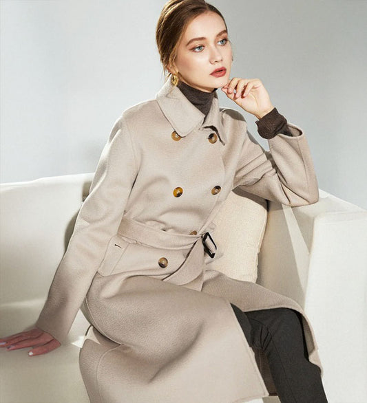 Model sitting on a sofa in the Pearl Bush structured wool coat, mid-calf length visible. From Borcelleclothes.