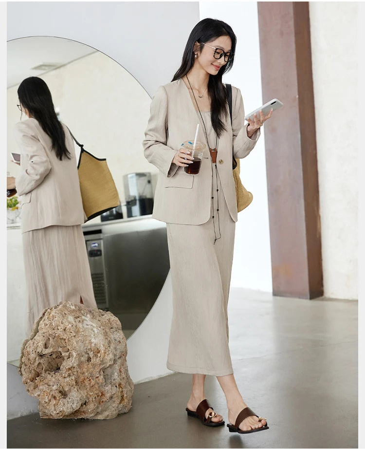 Model wearing Swiss Coffee set while looking at her phone — single-breasted jacket over a flowing camisole dress. From Borcelleclothes.