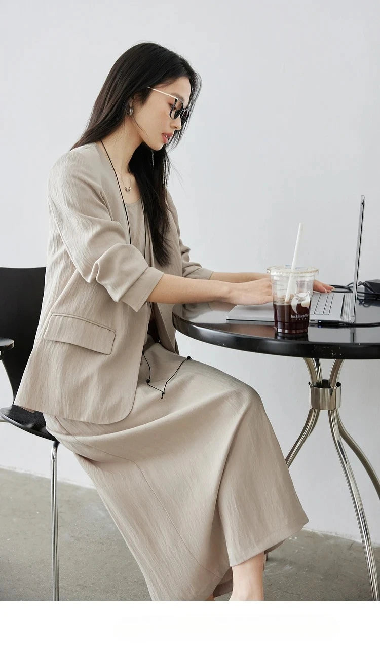 Woman typing on a notebook — clean lines of jacket and straps of the dress visible in a focused moment. From Borcelleclothes.