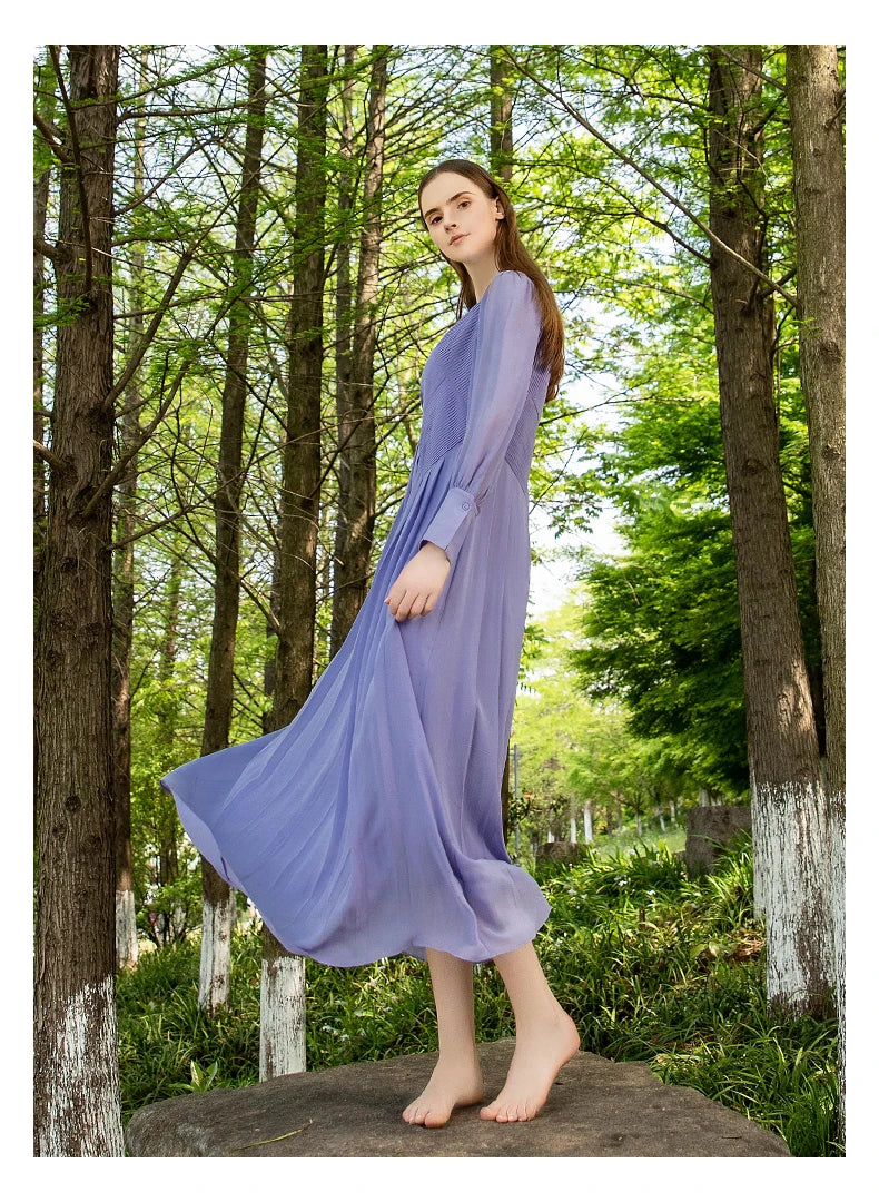 Side view of the model turning slowly among trees, revealing the layered tuck construction of the dress in filtered forest light. From Borcelleclothes.