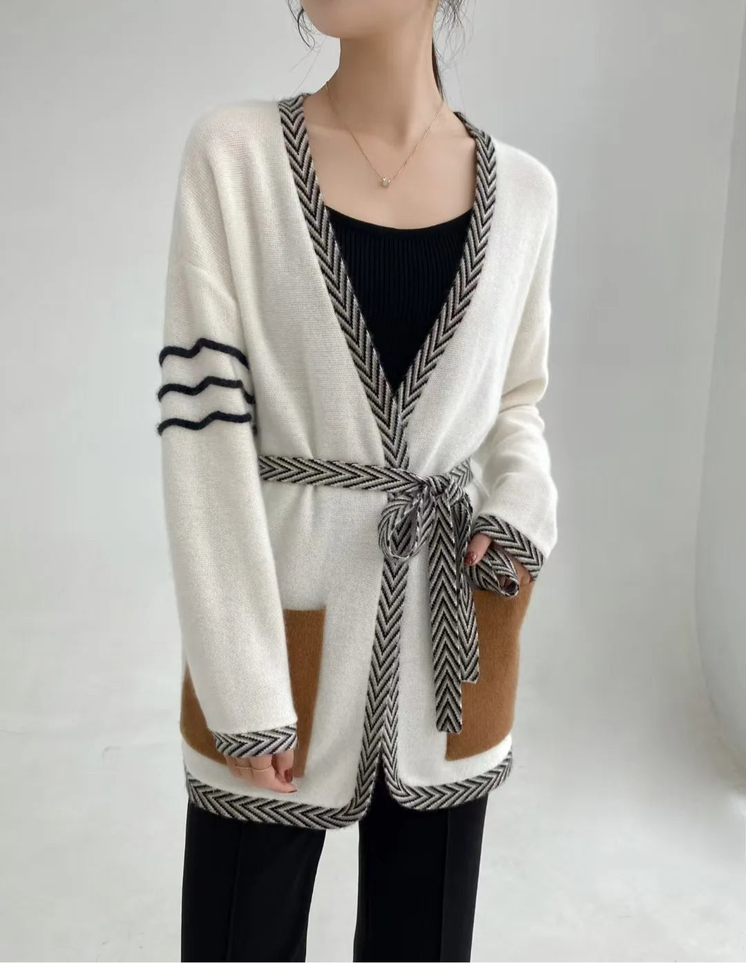 Whispering Smoke cashmere cardigan with model’s hand resting in the cardigan pocket, showing chevron trim and quiet definition — From Borcelleclothes.