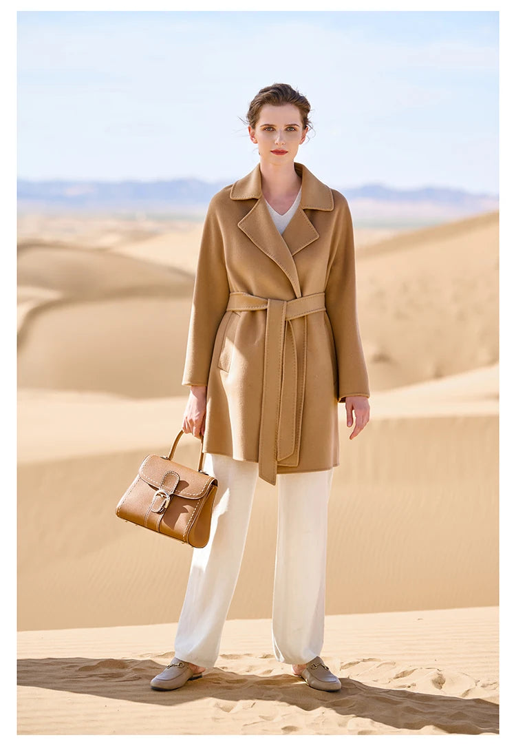 Model wearing a French Beige wrap cashmere coat, holding a bag. From Borcelleclothes.