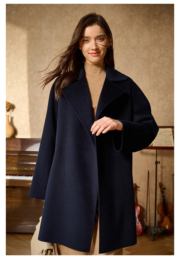 Model wearing a Mirage wrap cashmere coat, touching the front lapel. From Borcelleclothes.